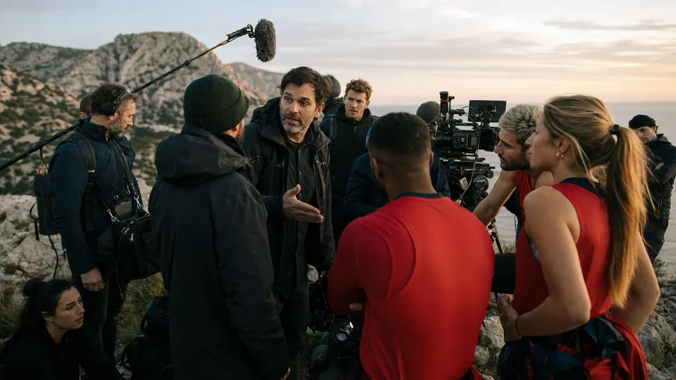 Illustrative photo of a reality TV crew and contestants gathered on a rocky coastline at dusk after a day of filming.