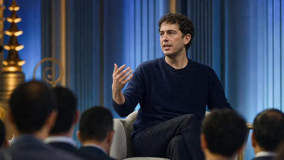 Illustrative photo of an AI company co-founder speaking on stage at an international economic conference, gesturing as he talks to a blurred audience.