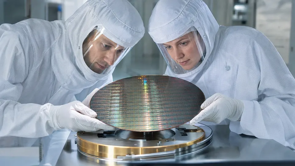 Two engineers in cleanroom suits examine a large wafer-scale processor on a lab table.