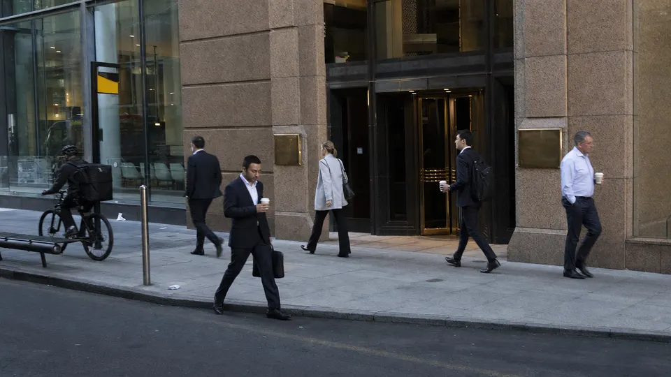 Office workers in business attire walk past the Australian Securities Exchange building in Sydney on a clear morning.
