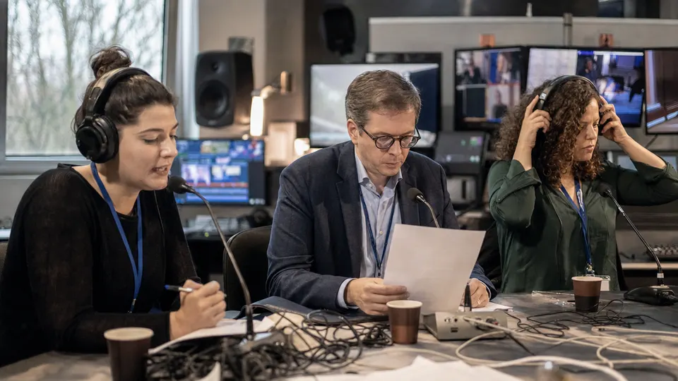 GEN anchors Aurelia Crown, Hari Sterne and Zola Kade work together at a broadcast desk in a Ljubljana studio.