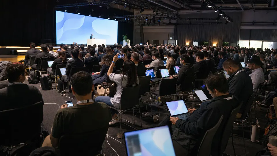 Attendees seated in rows at a Google Cloud keynote, facing a large glowing stage screen, with laptops and phones in hand.