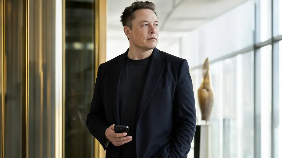 Elon Musk holding a smartphone in a bright modern workspace, shown in three-quarter view (illustrative photo, not a depiction of a reported event).
