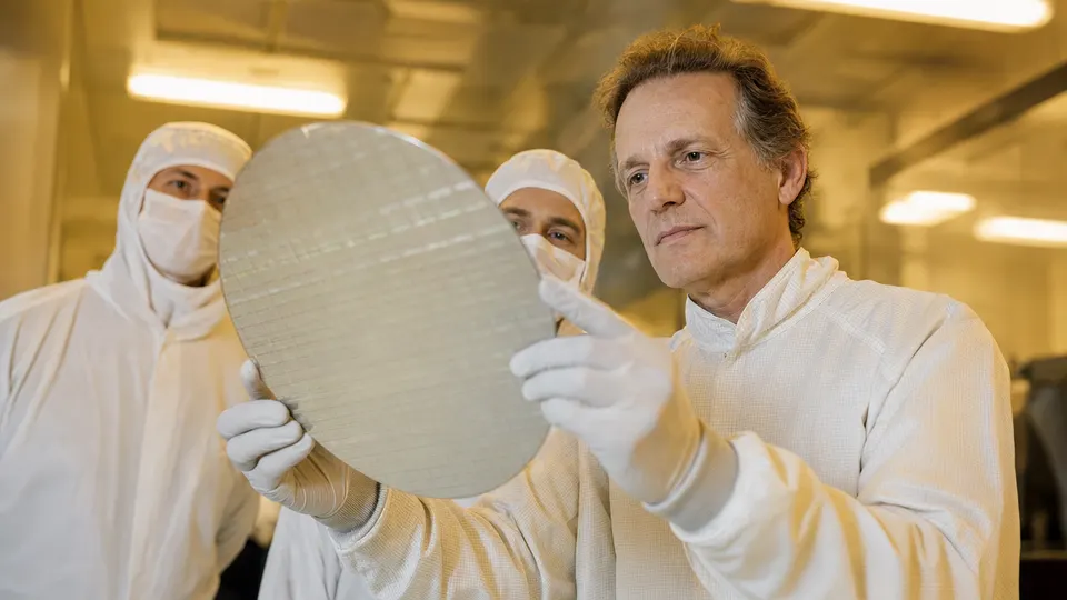 Infineon CEO Jochen Hanebeck holding a large silicon wafer in a cleanroom beside two engineers, in an illustrative photo
