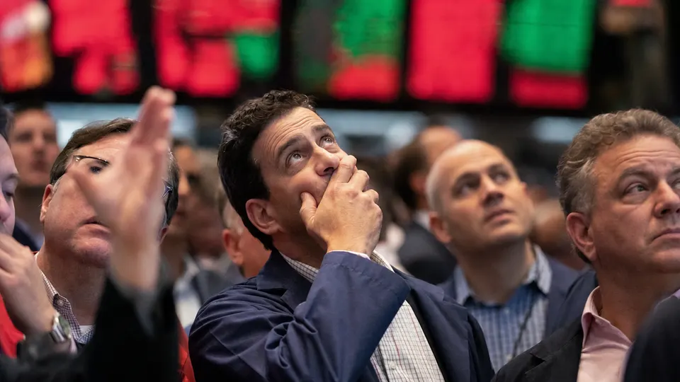Traders on a stock exchange floor react as screens glow red during a market sell-off