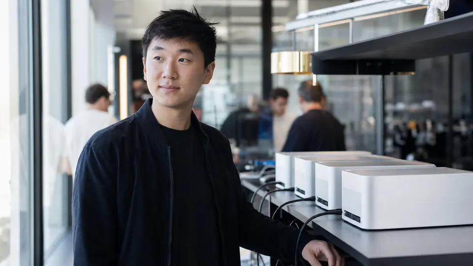 Illustrative photo of a Meta AI executive standing next to four connected compact desktop computers in a bright lab.