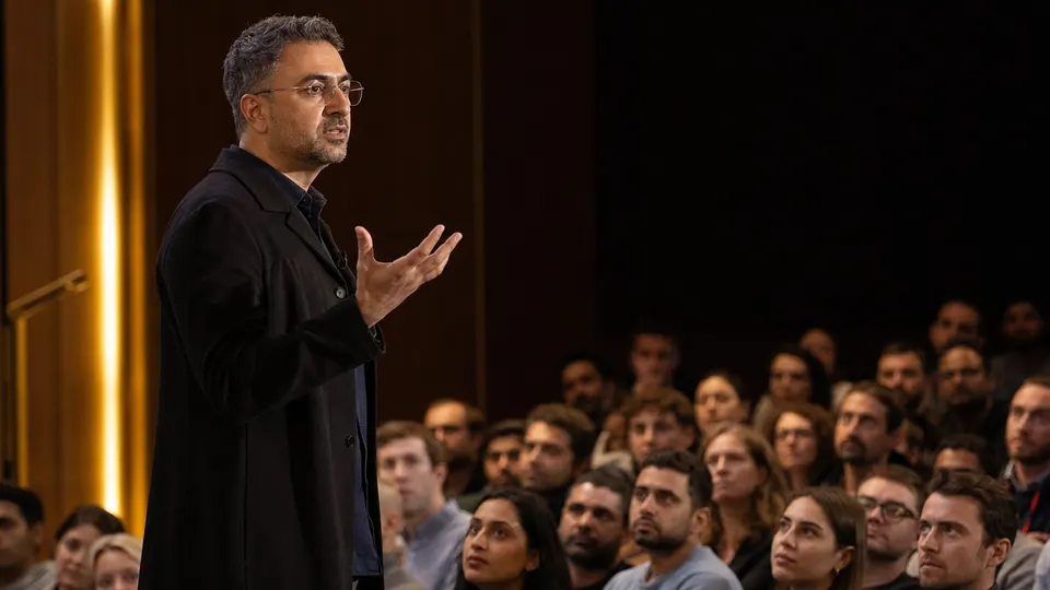Illustrative photo of a Microsoft AI executive addressing employees at a company town hall, with engineers listening in the foreground.