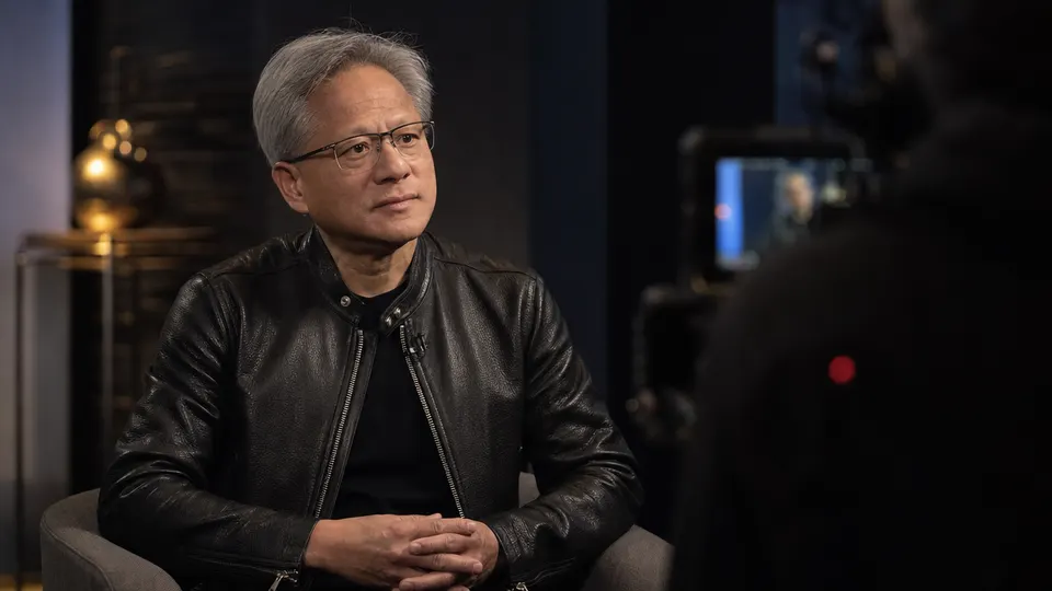 Illustrative photo of Nvidia CEO Jensen Huang seated in a studio interview setting, looking attentively off-camera.