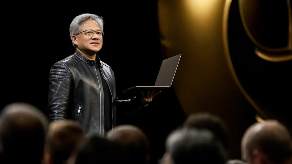 Illustrative photo of a technology executive on a keynote stage holding up a laptop toward an audience.