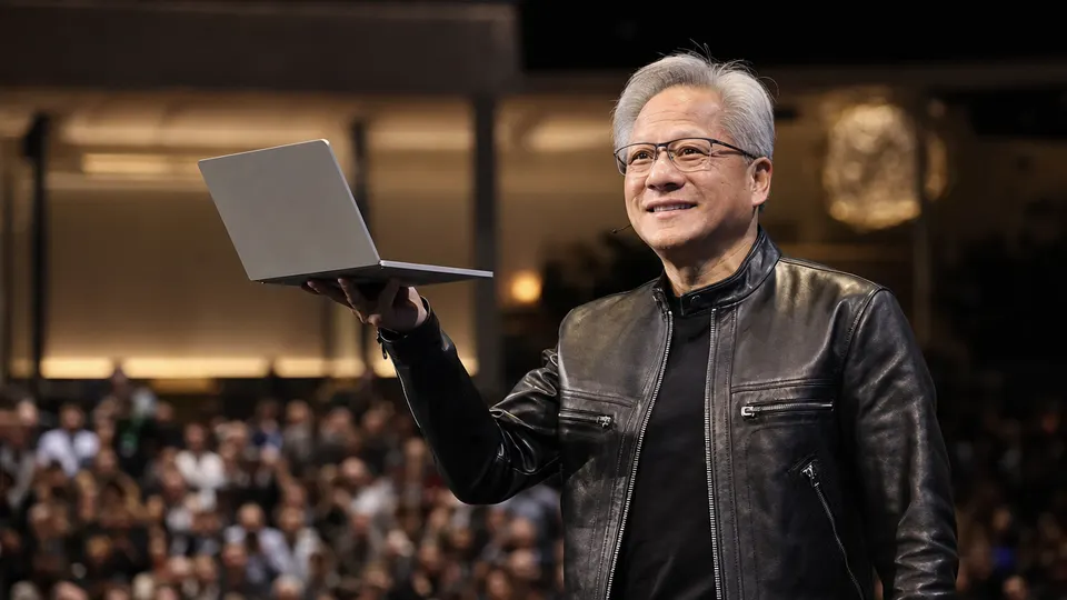 Jensen Huang holding a thin laptop on a keynote stage, lit by warm stage lights