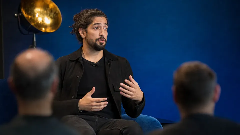A tech CEO speaking on a conference stage in front of an attentive audience of startup founders.